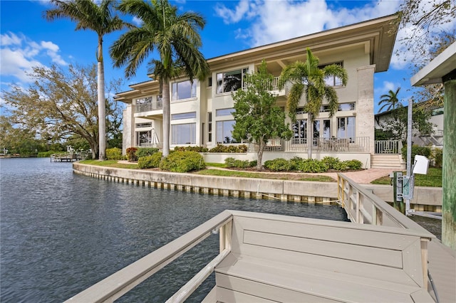 back of house with stucco siding, a water view, and a balcony