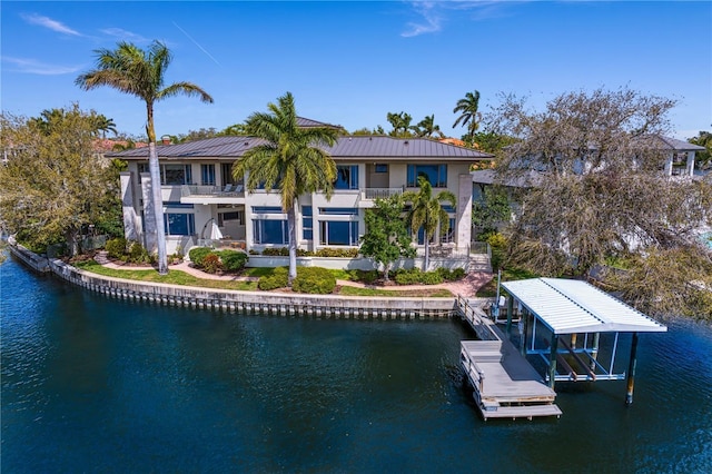 rear view of house with a balcony, a standing seam roof, a water view, boat lift, and metal roof