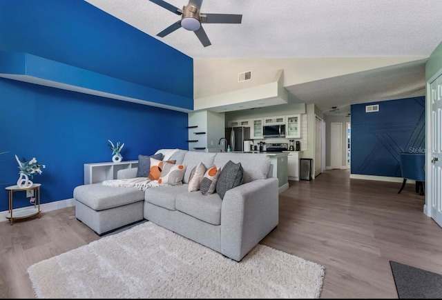 living area featuring wood finished floors, baseboards, visible vents, ceiling fan, and vaulted ceiling