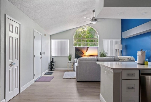 interior space with baseboards, ceiling fan, light wood-type flooring, vaulted ceiling, and a textured ceiling