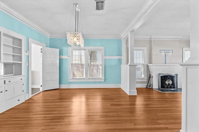 unfurnished living room with built in features, wood finished floors, decorative columns, crown molding, and a brick fireplace