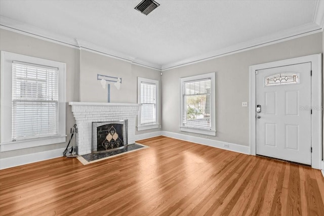 unfurnished living room with visible vents, baseboards, ornamental molding, a fireplace, and light wood-style floors