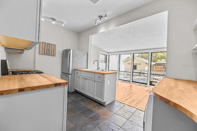 kitchen featuring a sink, wood counters, stone tile flooring, freestanding refrigerator, and rail lighting