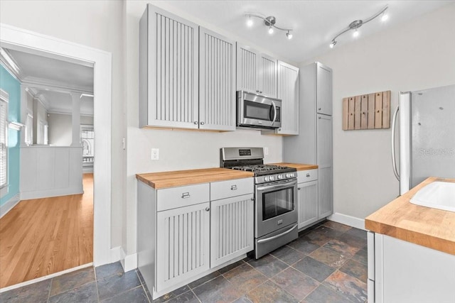 kitchen with butcher block counters, stone finish flooring, baseboards, and stainless steel appliances