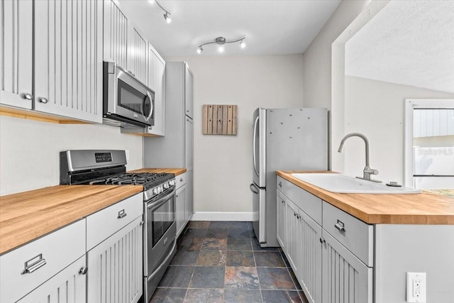 kitchen with baseboards, a sink, stone finish floor, appliances with stainless steel finishes, and wood counters