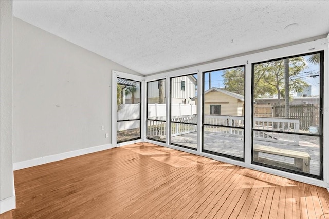 unfurnished room featuring a textured ceiling, baseboards, lofted ceiling, and wood-type flooring