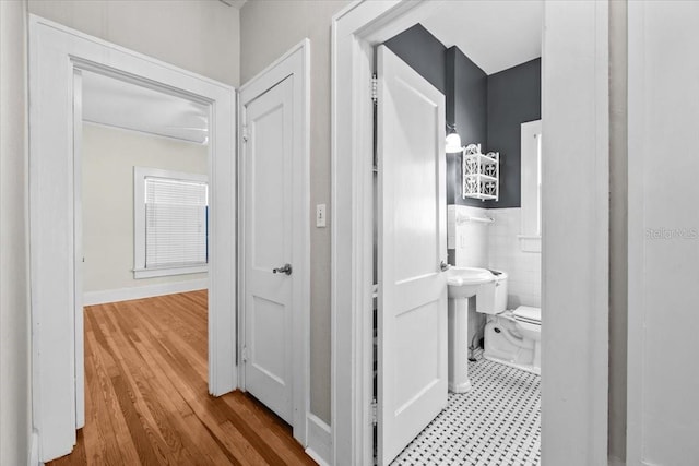 hallway with tile walls, wood finished floors, and wainscoting