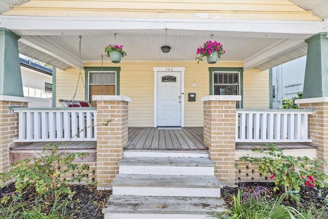 view of exterior entry with brick siding and a porch