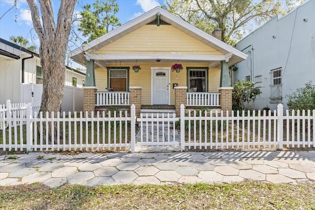 view of front facade with a fenced front yard, brick siding, a porch, and a chimney