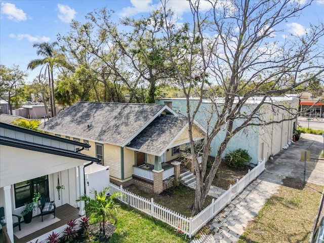 exterior space with a fenced front yard, roof with shingles, and covered porch