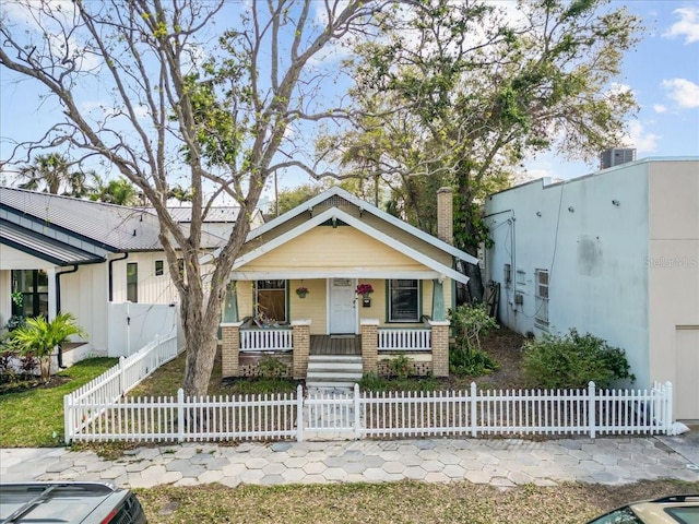 view of front facade featuring a fenced front yard, covered porch, a chimney, and a gate