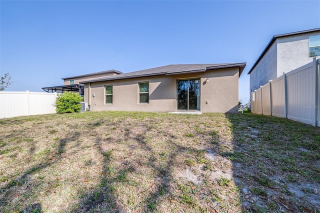 rear view of property featuring stucco siding, a lawn, and fence