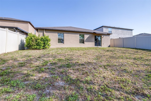 back of house featuring a fenced backyard, a lawn, and stucco siding