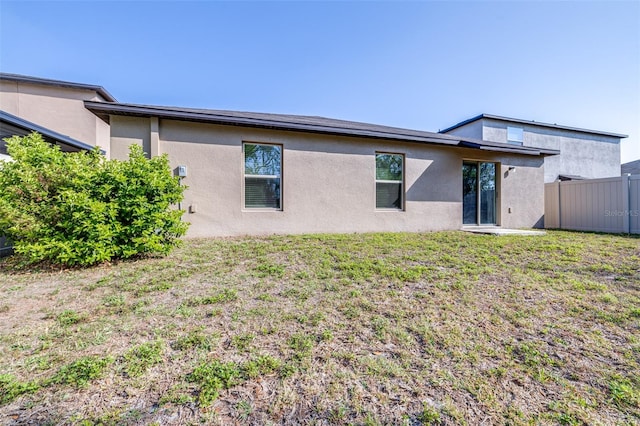 rear view of property with a yard, fence, and stucco siding