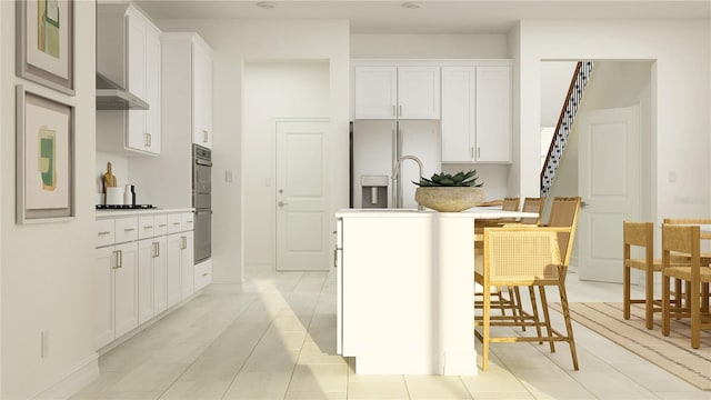 kitchen featuring ventilation hood, an island with sink, white cabinetry, double oven, and fridge with ice dispenser