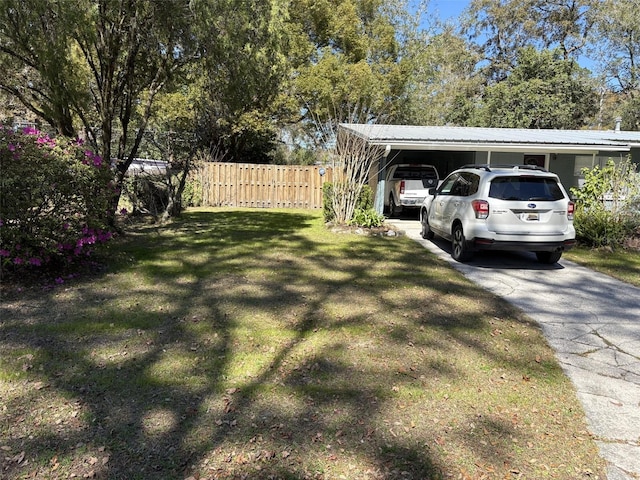 view of yard featuring a carport, concrete driveway, and fence