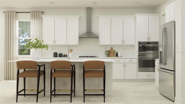 kitchen featuring wall chimney range hood, an island with sink, light countertops, white cabinets, and stainless steel appliances