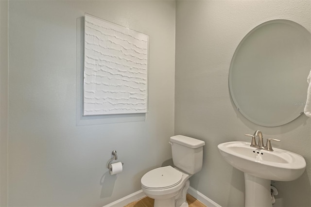 half bathroom featuring baseboards, toilet, and wood finished floors