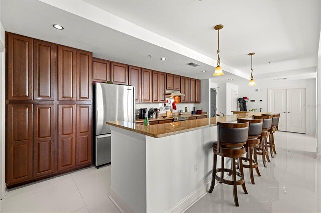 kitchen featuring under cabinet range hood, freestanding refrigerator, recessed lighting, a breakfast bar area, and light tile patterned floors