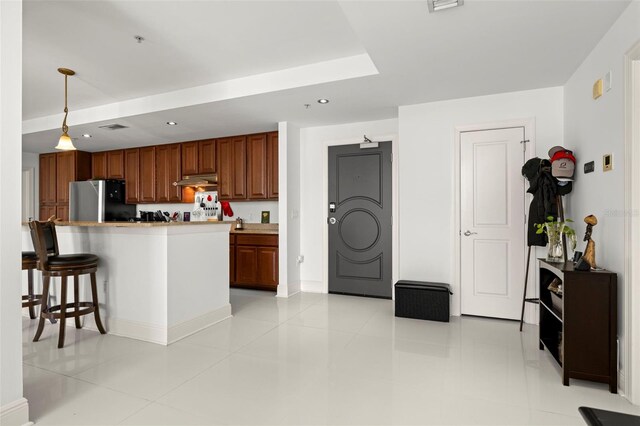 kitchen with brown cabinets, a breakfast bar, freestanding refrigerator, recessed lighting, and hanging light fixtures