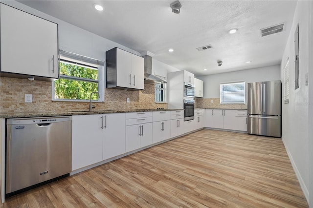 kitchen featuring a sink, stainless steel appliances, visible vents, and wall chimney range hood