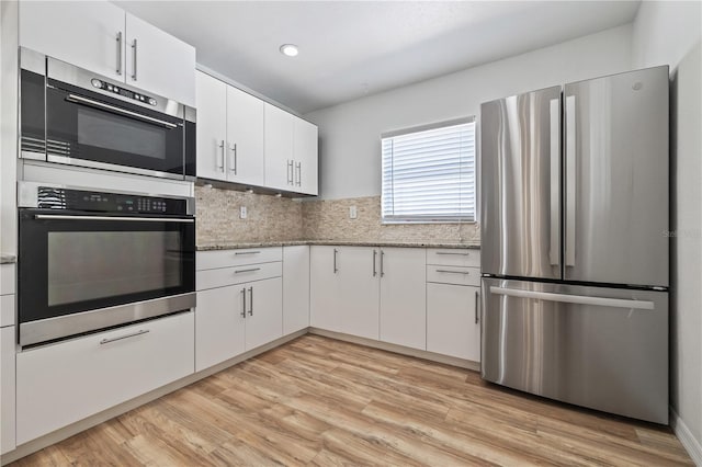 kitchen with light wood finished floors, white cabinets, light stone countertops, and freestanding refrigerator