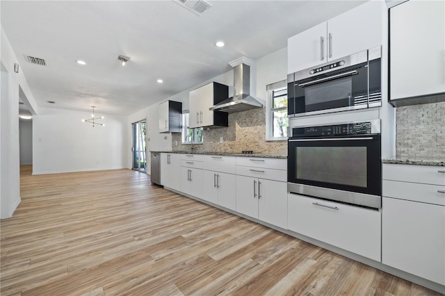 kitchen featuring visible vents, backsplash, wall chimney exhaust hood, and light wood finished floors