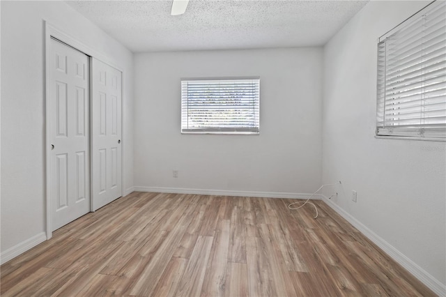 unfurnished bedroom featuring light wood-style flooring, baseboards, a closet, and a textured ceiling