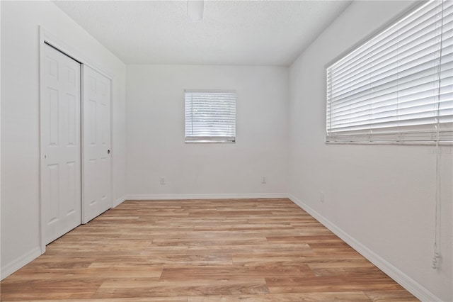 unfurnished bedroom featuring baseboards, light wood-type flooring, a closet, and a textured ceiling