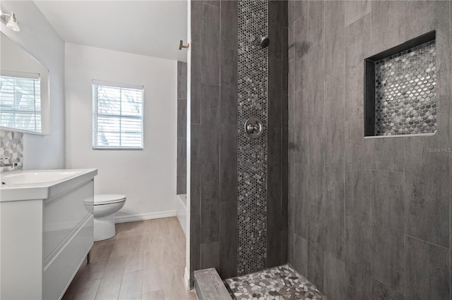 full bath with tiled shower, toilet, wood finished floors, and vanity