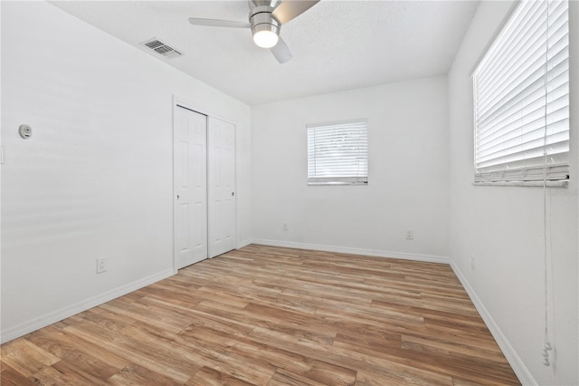 unfurnished bedroom featuring baseboards, visible vents, a closet, a textured ceiling, and light wood-type flooring