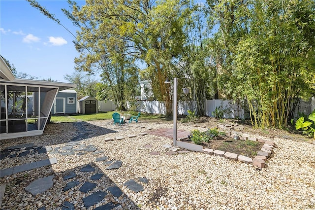 view of yard featuring a storage unit, fence, an outdoor structure, and a sunroom