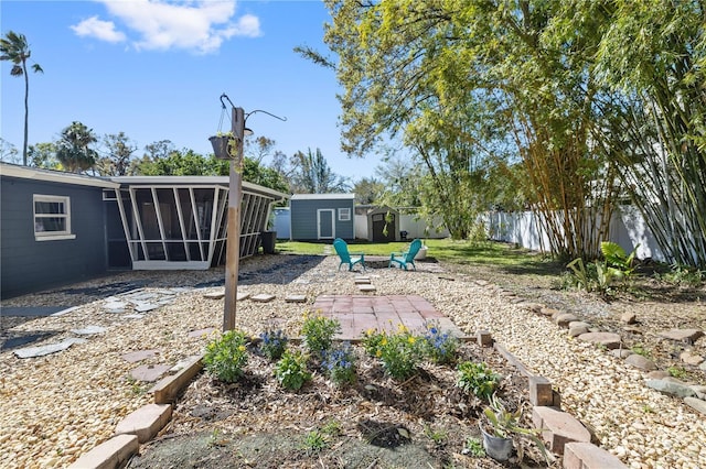 view of yard with a fire pit, fence, a storage shed, a sunroom, and an outbuilding