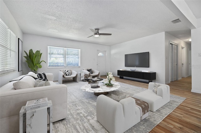 living area featuring visible vents, a textured ceiling, wood finished floors, baseboards, and ceiling fan