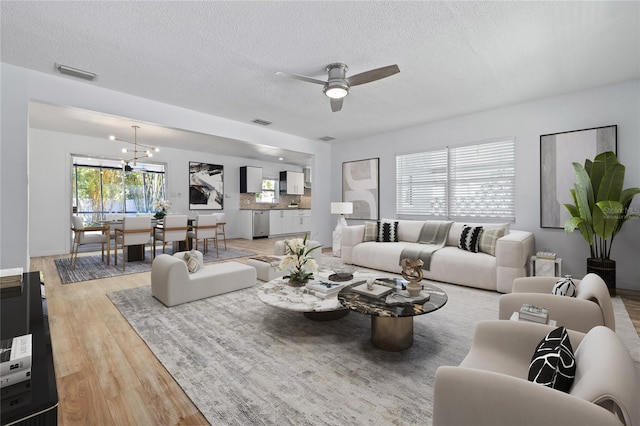 living room with light wood-type flooring, visible vents, a textured ceiling, and ceiling fan with notable chandelier