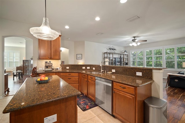 kitchen with brown cabinetry, dishwasher, a peninsula, arched walkways, and a sink