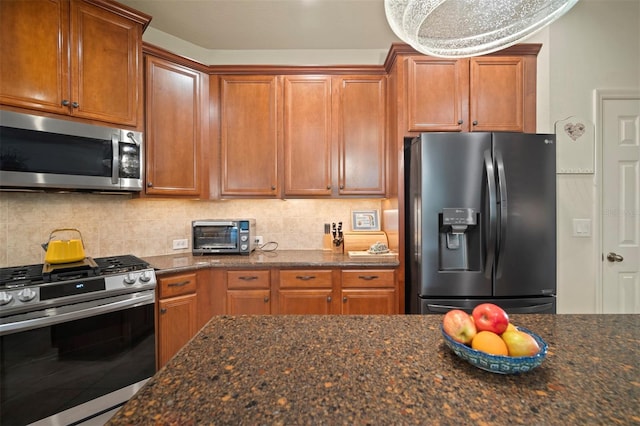 kitchen featuring dark stone countertops, brown cabinetry, a toaster, appliances with stainless steel finishes, and tasteful backsplash