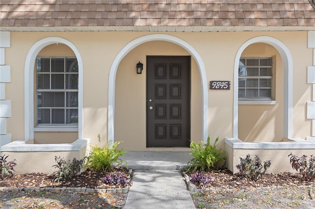 view of exterior entry featuring stucco siding and a shingled roof