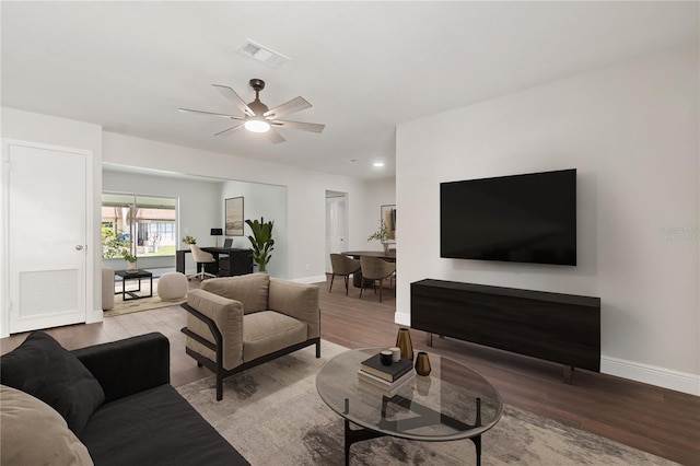 living room featuring ceiling fan, visible vents, baseboards, and wood finished floors