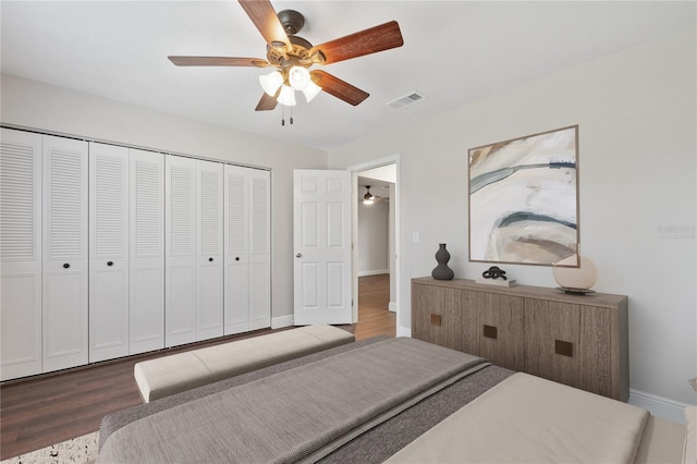 bedroom with a ceiling fan, wood finished floors, visible vents, baseboards, and a closet