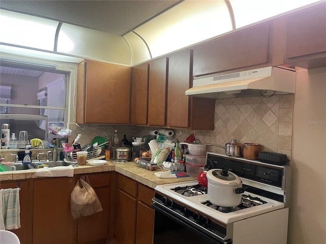 kitchen with under cabinet range hood, a sink, decorative backsplash, and white gas range oven