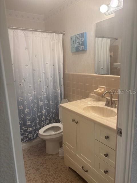 bathroom with toilet, vanity, wainscoting, a shower with curtain, and tile walls