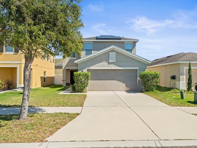 traditional-style home with stucco siding, driveway, a front lawn, roof mounted solar panels, and a garage