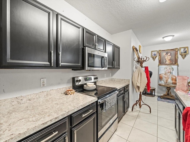 kitchen featuring a textured ceiling, stainless steel appliances, light countertops, light tile patterned floors, and dark cabinets