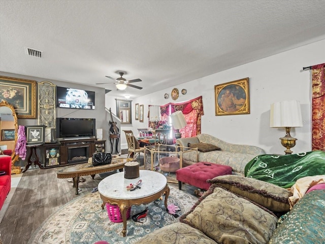 living area with ceiling fan, wood finished floors, visible vents, and a textured ceiling