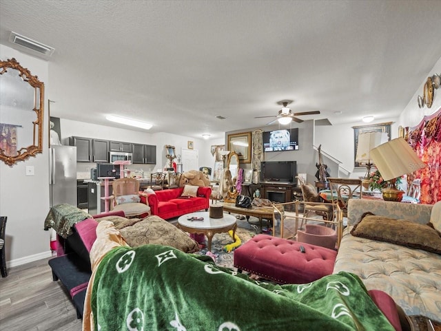 living area with visible vents, baseboards, light wood-style floors, a textured ceiling, and a ceiling fan