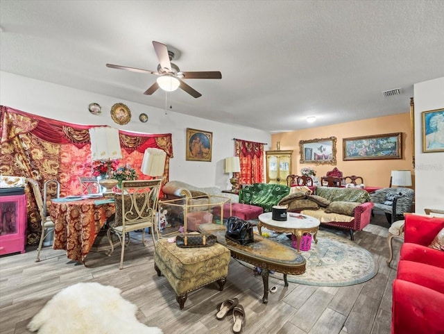 living area featuring ceiling fan, visible vents, a textured ceiling, and wood finished floors