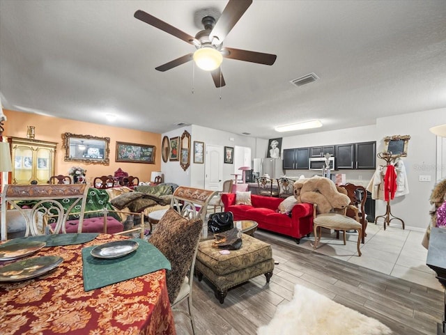 living room with a textured ceiling, light wood-style flooring, visible vents, and ceiling fan