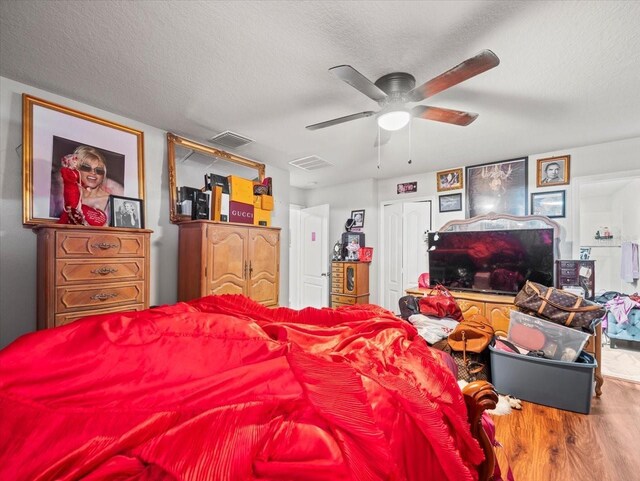 bedroom featuring a ceiling fan, wood finished floors, visible vents, and a textured ceiling