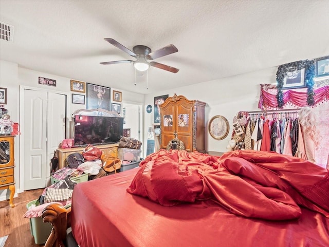 bedroom featuring a ceiling fan, wood finished floors, visible vents, and a textured ceiling